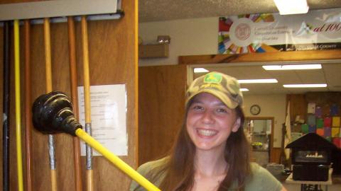 camper smiling for the camera with a plunger in hand 