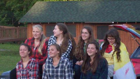 Cabin group wearing plaid sitting on picnic table smiling.