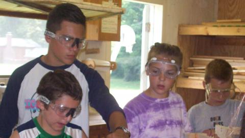 Campers working on wood shop projects with the help of an older youth.