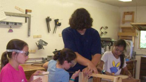 campers working on wood shop projects with the help of an adult. 