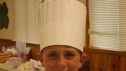 Camper holding culinary creation and wearing a chef's hat.