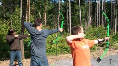 Archery youth stand on the firing line with their bows drawn prepared to fire.