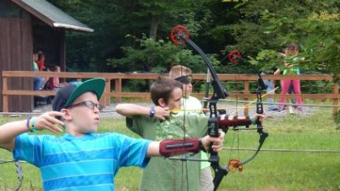 Youth lined up shooting bow and arrows. 