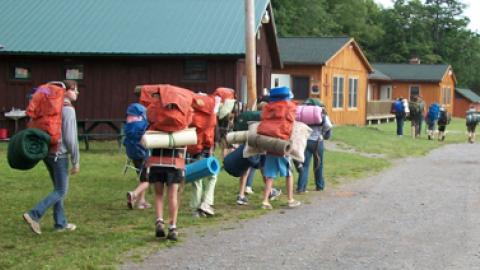 Group of youth walking off toward the woods with packed bags for a camp-out in Lennox Forest.