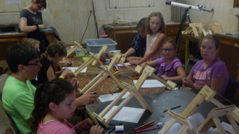 youth gathered around a table stringing beads onto wooden looms.