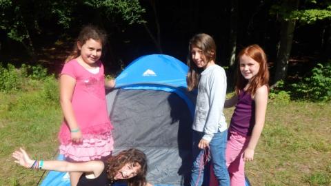 Youth smiling while standing in front of a small tent. 