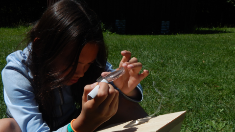 camper using a magnifying glass to burn a design into their wooden butterfly house.