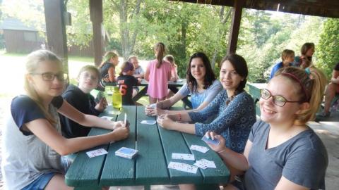 campers sit at a picnic table and play a card game 