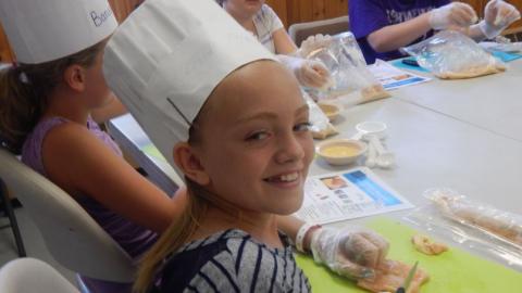 Camper participating in the cooking program smiles for the camera while wearing a chef's hat. 