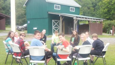 Youth sitting in chairs outside at camp. 