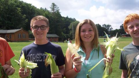 Youth hold up corn and the husks. 