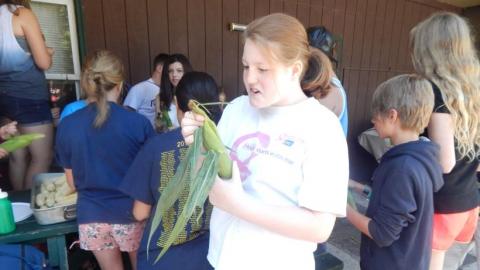 camper shucks an ear of corn with campers in the background 