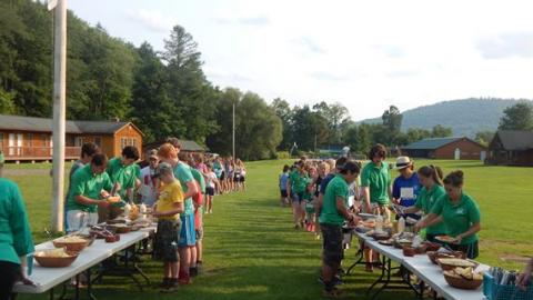 Campers and counselors fill their plates from the dinner tables on the camp field. 