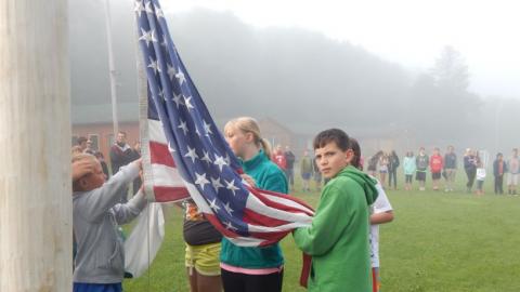 Youth lowering the flag with campers in the background. 