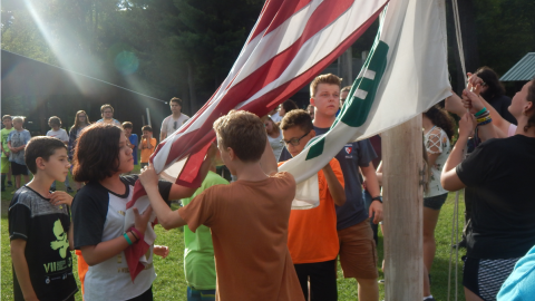 Campers work together to raise the 4-H and American flags while the rest of camp looks on.