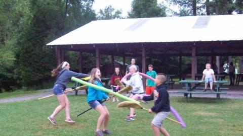 Campers playing a silly game with brooms and pool noodles. 