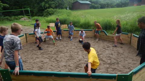 youth in gaga pit with one hand on the wall as the game begins.
