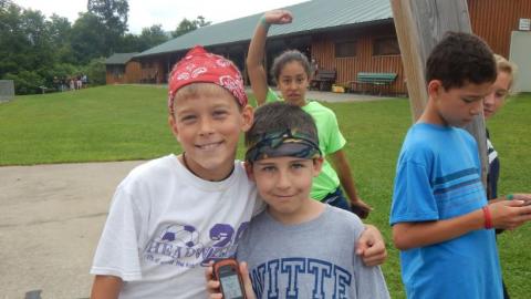 Campers pose with their geocaching device. Camper in the background with hand in the air. 