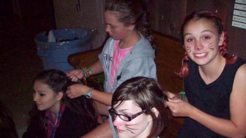 Youth braiding hair and wearing cat face paint. 