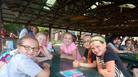 Youth smiling and sitting at a picnic table in the pavilion. 