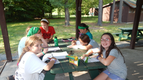 Campers seated at a picnic table coloring and drawing.