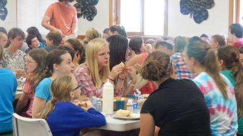 Youth sit at a table in the dining hall and eat a meal. 