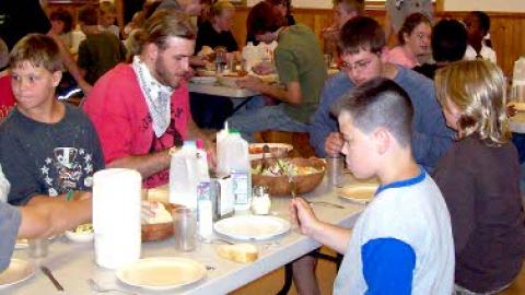 campers seated for a meal in the dining hall. Food is being served family style with a counselor seated at each table.