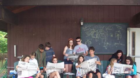 Campers sitting in chairs and reading newspapers. 
