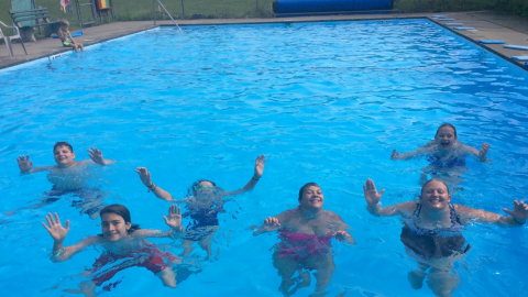 youth pose in the pool with hands raised above their head.