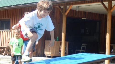 Youth jumps over a picnic table as part of a relay race. 