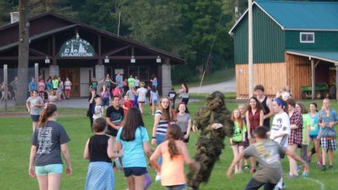group of campers watching and running from a person dressed in a jungle costume