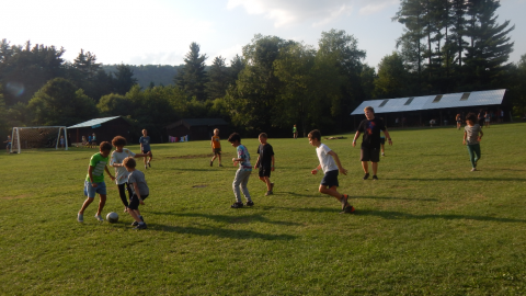 youth and counselor in field kicking a soccer ball.