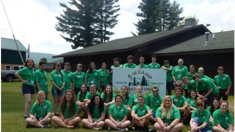 Camp staff pose for a photo in front of the 4-H Camp Shankitunk sign. 