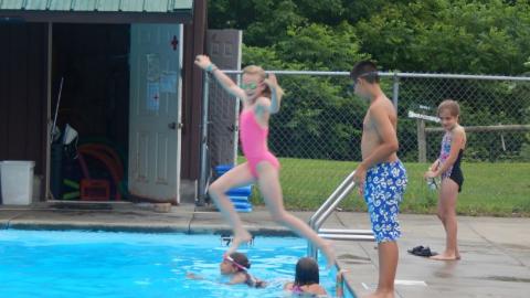 Youth jumping into the camp swimming pool with others in the background. 