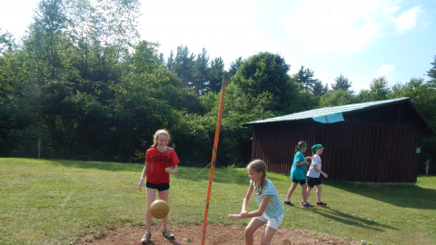 Two youth playing tether ball with two youth walking past in the background.
