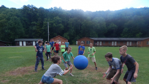Youth playing ultimate 4-square in the field. Large line in background of those waiting to play.