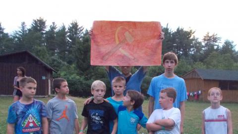 campers holds paper Russian flag in the air while other campers pose in front of it 