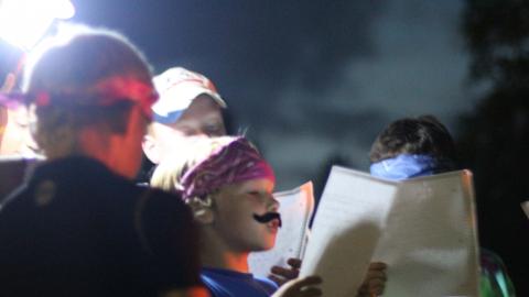 youth reading papers wearing bandanna and fake mustache 