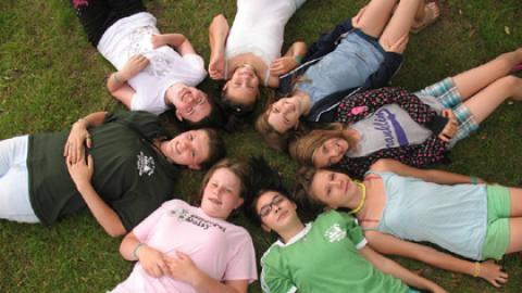Group of campers and their cabin counselors lay on the ground with their heads together in a circle.