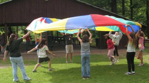 Group of campers play a game together with a parachute.