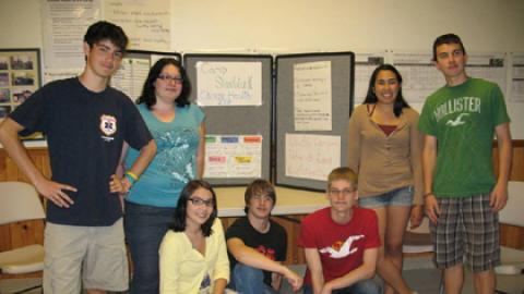 Group of counselor in training participants stand with a display board on choosing health at camp.