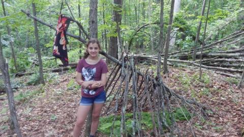Youth stands by the start of a shelter in the woods. 