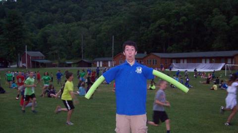 Counselor takes a silly photo with pool noodles as arms. 