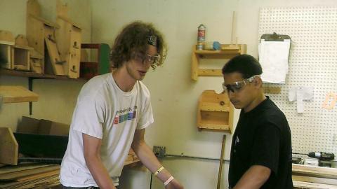 camper uses table saw in the camp wood shop with the help of a counselor.